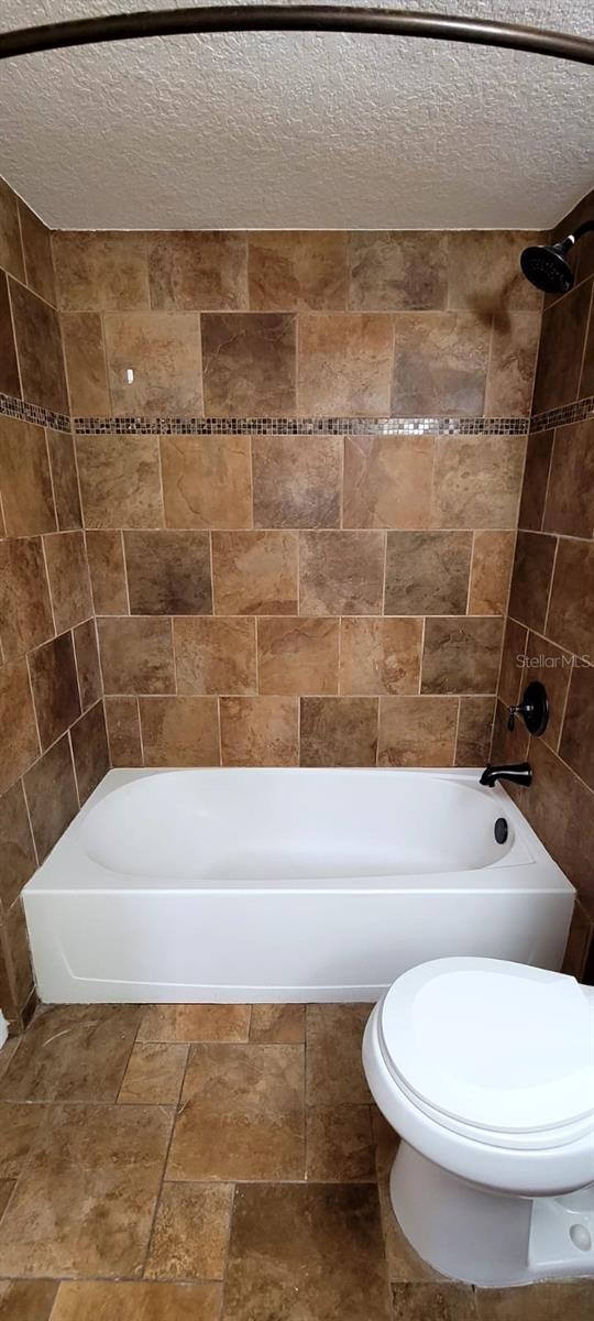 14049 Fairway Island Dr Unit 118, Orlando, FL 32837 - bathroom featuring toilet, stone finish flooring, a textured ceiling, and tub / shower combination