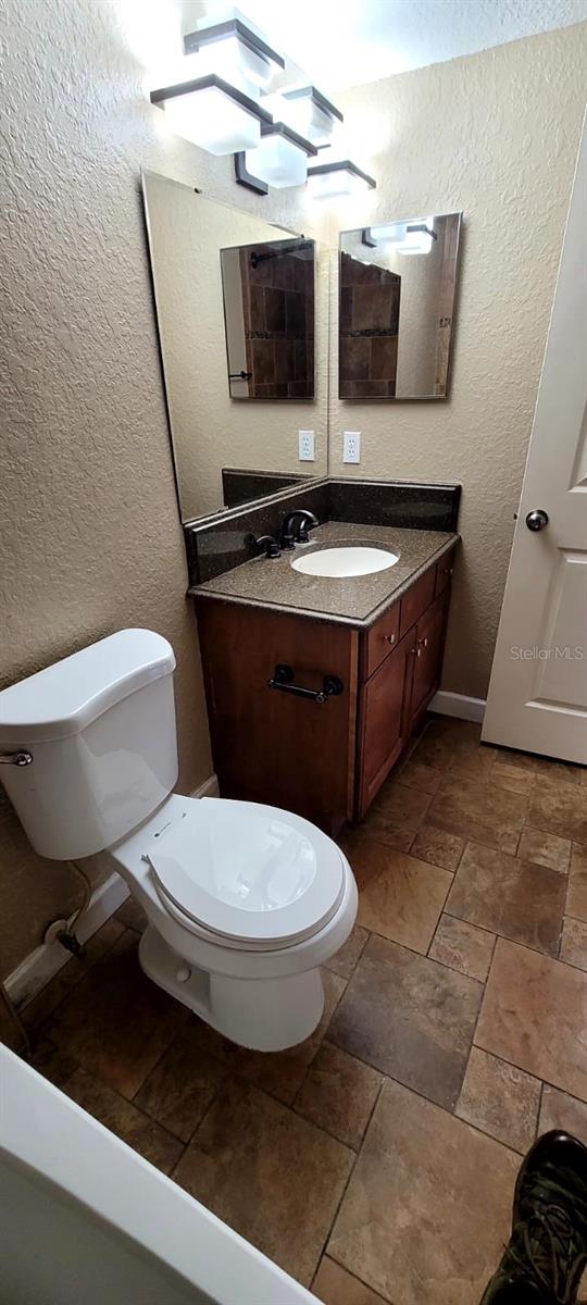 14049 Fairway Island Dr Unit 118, Orlando, FL 32837 - bathroom with vanity, a textured wall, stone tile flooring, and toilet