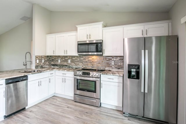 kitchen featuring light stone countertops, appliances with stainless steel finishes, a sink, lofted ceiling, and tasteful backsplash