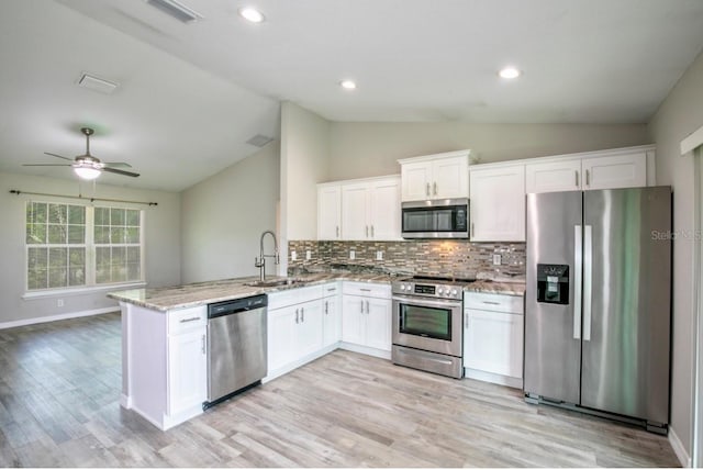 kitchen featuring visible vents, a peninsula, lofted ceiling, a sink, and appliances with stainless steel finishes