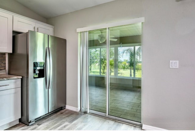 kitchen with stainless steel refrigerator with ice dispenser, white cabinets, light stone counters, a ceiling fan, and light wood finished floors