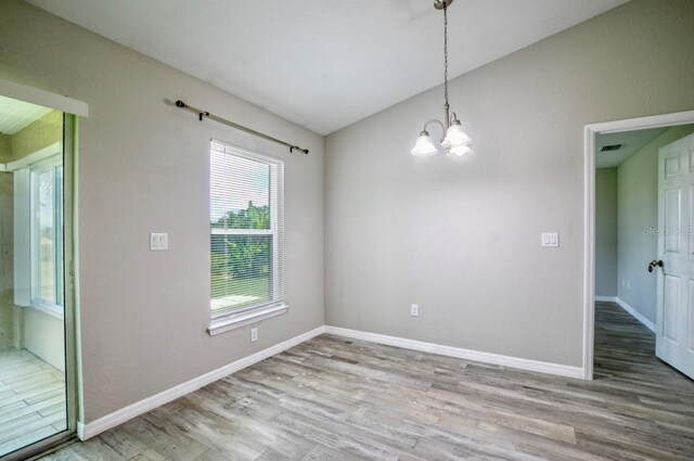 unfurnished room with an inviting chandelier, visible vents, wood finished floors, baseboards, and vaulted ceiling