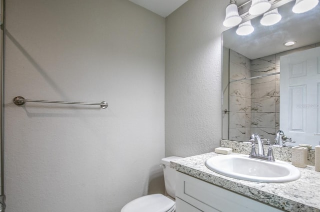 bathroom featuring toilet, a textured wall, a shower, and vanity