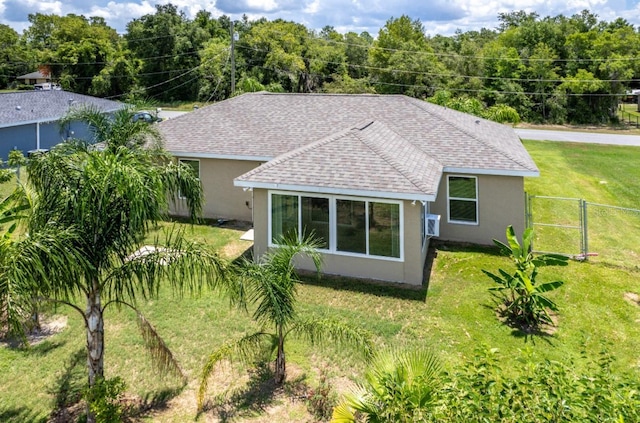 rear view of house featuring fence, a shingled roof, stucco siding, a gate, and a lawn