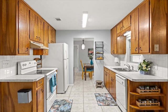 kitchen featuring brown cabinets, a sink, white appliances, light countertops, and under cabinet range hood