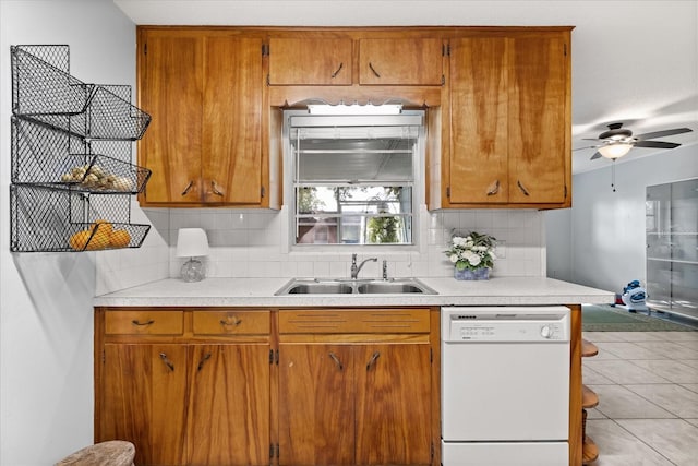 kitchen with brown cabinetry, white dishwasher, light countertops, tasteful backsplash, and a sink