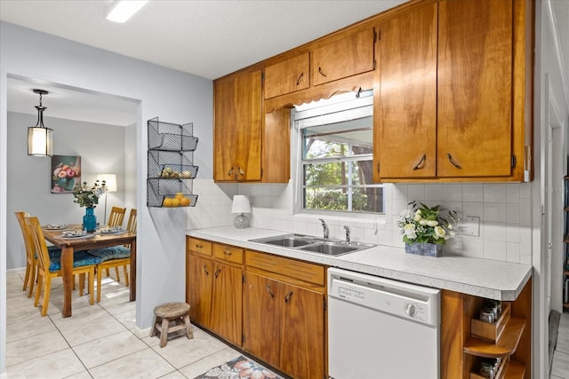kitchen featuring brown cabinetry, decorative backsplash, white dishwasher, light countertops, and a sink