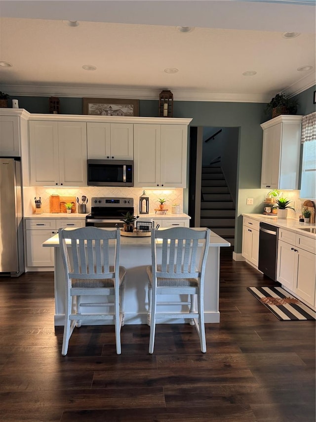 kitchen featuring appliances with stainless steel finishes, a breakfast bar area, white cabinets, backsplash, and ornamental molding