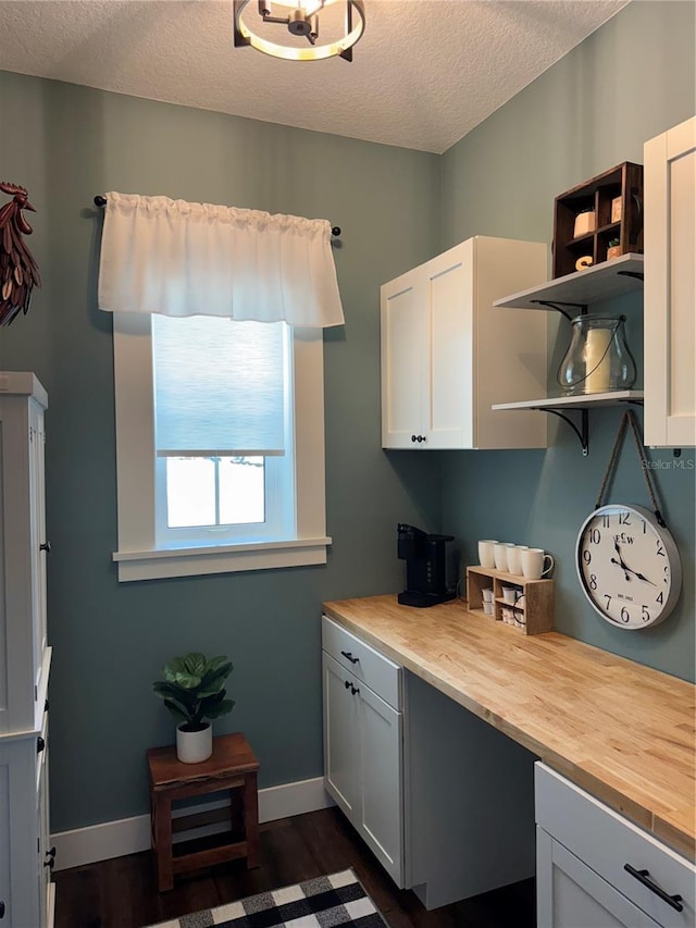 kitchen featuring dark wood-style flooring, a textured ceiling, open shelves, baseboards, and wood counters