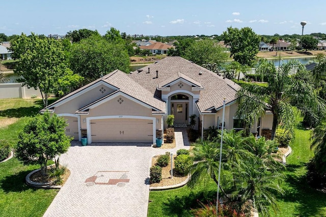 view of front facade featuring a front lawn, decorative driveway, roof with shingles, stucco siding, and an attached garage