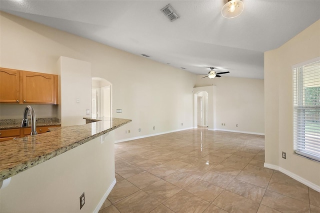 unfurnished living room with baseboards, arched walkways, a ceiling fan, and visible vents