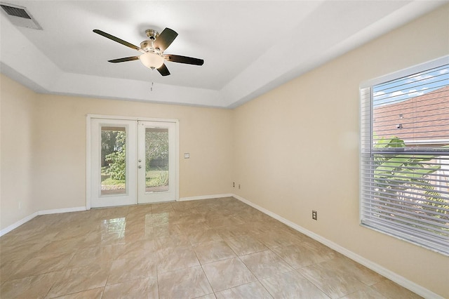 unfurnished room with a tray ceiling, a ceiling fan, and plenty of natural light
