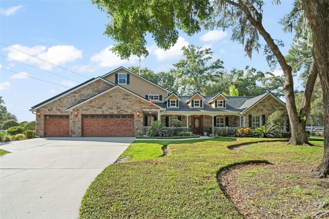 view of front of house with stone siding, a garage, a porch, a front yard, and concrete driveway