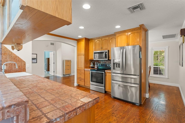 kitchen with stainless steel appliances, visible vents, dark wood-style floors, and a sink