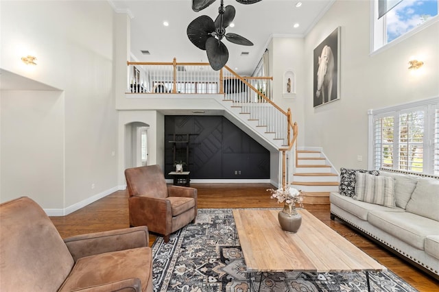 living area featuring stairs, ceiling fan, wood finished floors, and a towering ceiling
