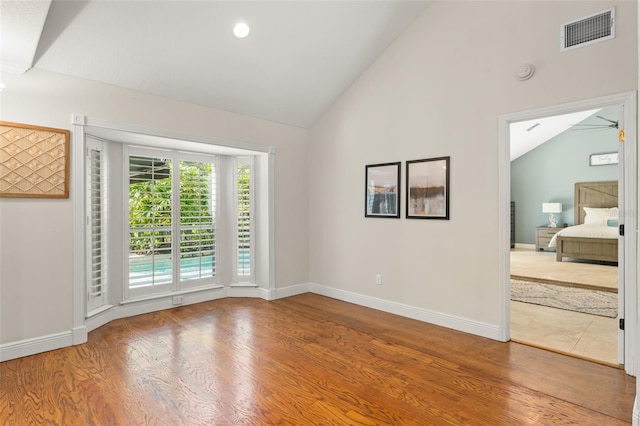 empty room with baseboards, high vaulted ceiling, wood finished floors, and visible vents