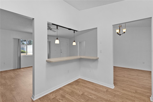 interior space with light countertops, a textured ceiling, ceiling fan with notable chandelier, wood finished floors, and pendant lighting