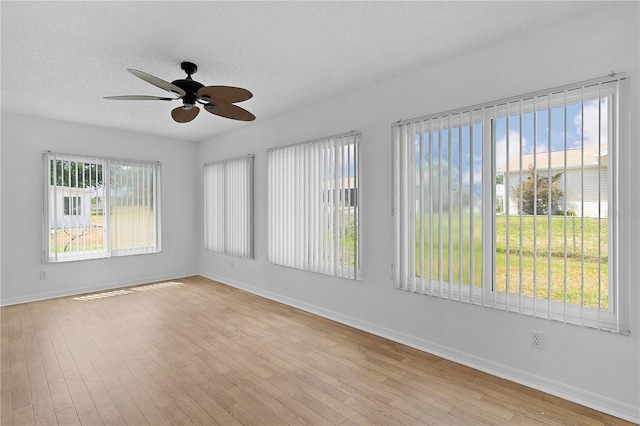 empty room featuring baseboards, a ceiling fan, light wood finished floors, and a textured ceiling