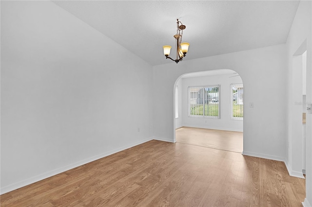 spare room with arched walkways, baseboards, light wood-style flooring, and a chandelier