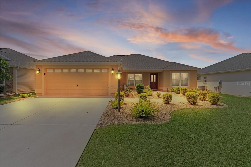 5596 Cedar Waxwing Dr, The Villages, FL 32163 - view of front facade with an attached garage, a yard, stucco siding, and driveway