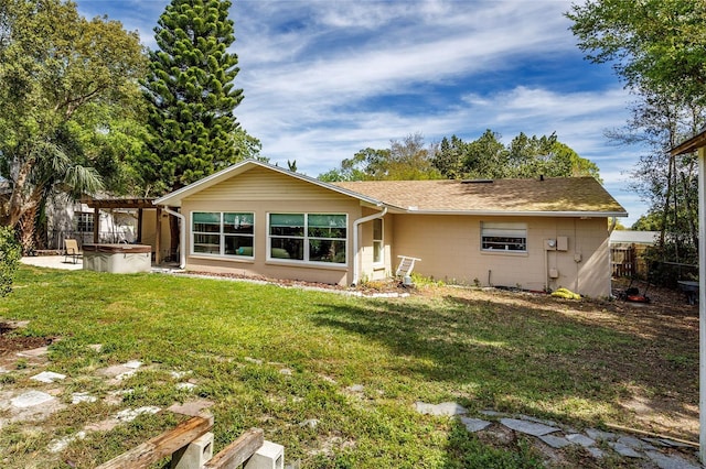 rear view of house featuring fence, a pergola, a hot tub, concrete block siding, and a yard