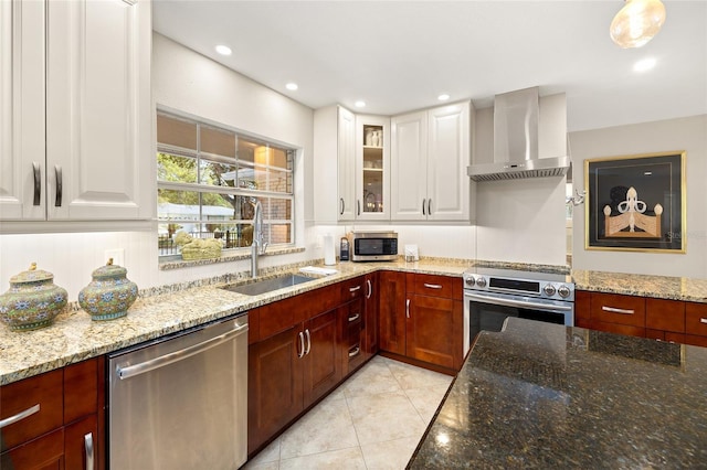 kitchen with wall chimney range hood, appliances with stainless steel finishes, light stone counters, a sink, and white cabinetry