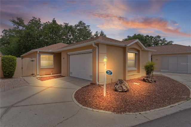 single story home with a gate, a garage, stucco siding, a shingled roof, and driveway