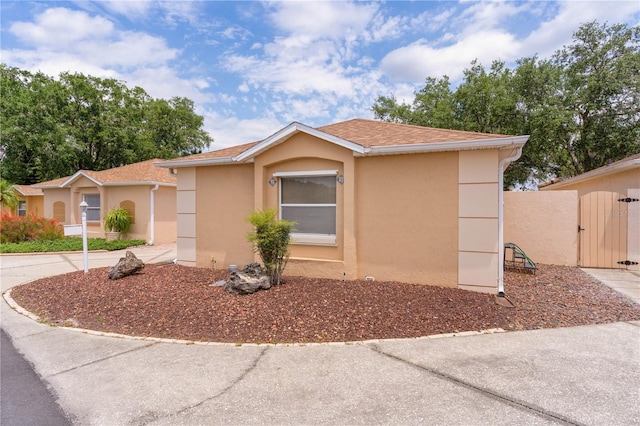 ranch-style house featuring a gate, roof with shingles, and stucco siding