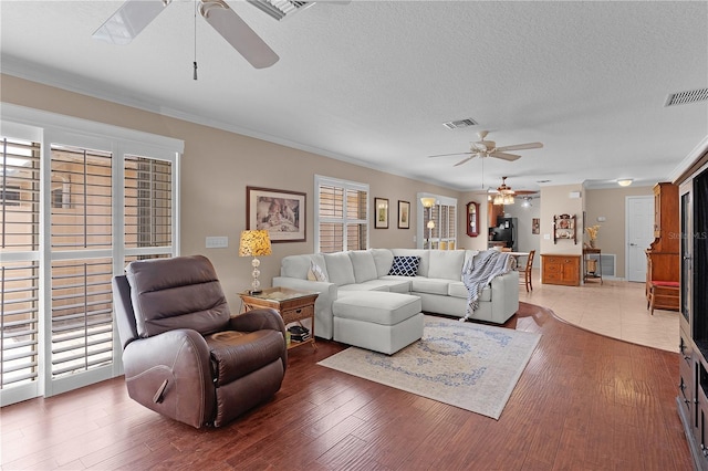 living area with a textured ceiling, a ceiling fan, and visible vents