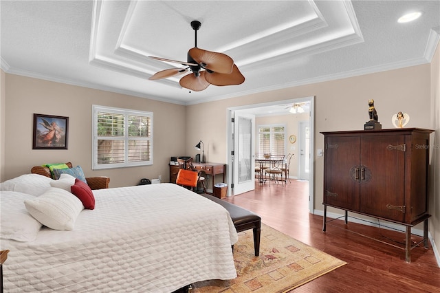 bedroom with a raised ceiling, multiple windows, and wood finished floors