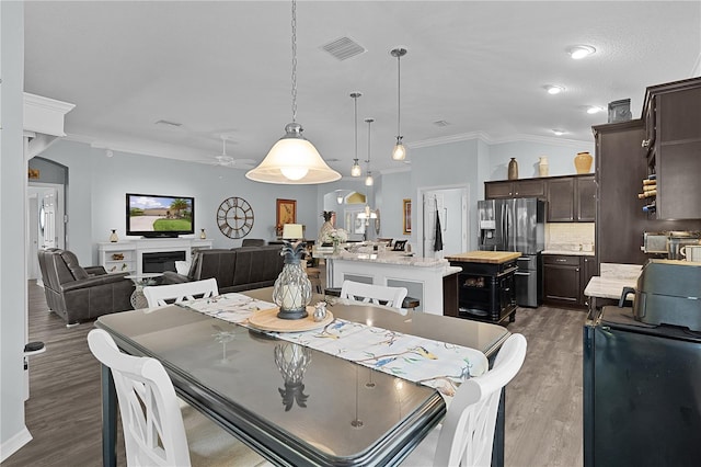 3433 Nestlebranch Ave, The Villages, FL 32163 - dining area featuring crown molding, ceiling fan, a glass covered fireplace, wood finished floors, and visible vents