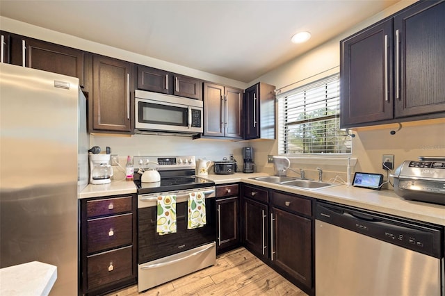 kitchen featuring dark brown cabinetry, appliances with stainless steel finishes, light wood-type flooring, a sink, and light countertops