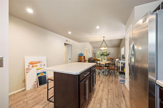 kitchen with freestanding refrigerator, a breakfast bar, light wood-type flooring, a center island, and light countertops
