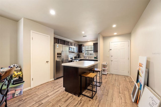 kitchen featuring a breakfast bar area, a kitchen island, appliances with stainless steel finishes, light countertops, and light wood-style floors