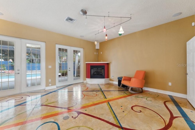 unfurnished living room with baseboards, visible vents, track lighting, and french doors