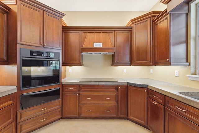 kitchen featuring brown cabinets, light countertops, black oven, cooktop, and a warming drawer