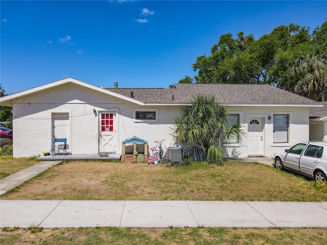 ranch-style home featuring stucco siding, roof with shingles, a front lawn, and cooling unit
