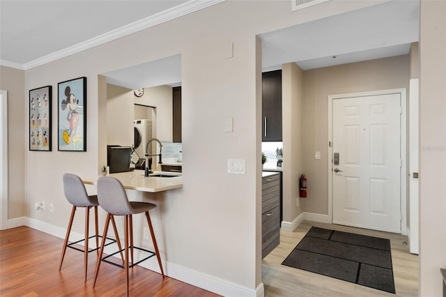 kitchen with baseboards, a sink, a kitchen bar, light wood-style floors, and light countertops