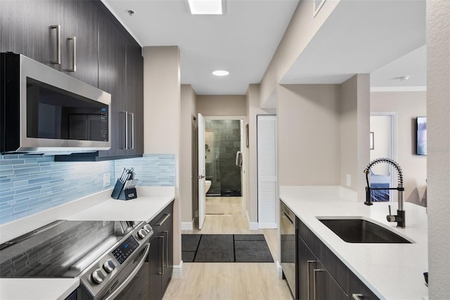 kitchen featuring a sink, stainless steel appliances, light countertops, light wood-style floors, and decorative backsplash