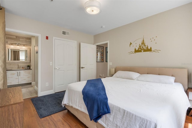 bedroom featuring baseboards, connected bathroom, visible vents, and wood finished floors