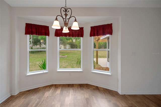 unfurnished dining area with wood finished floors, plenty of natural light, a chandelier, and baseboards