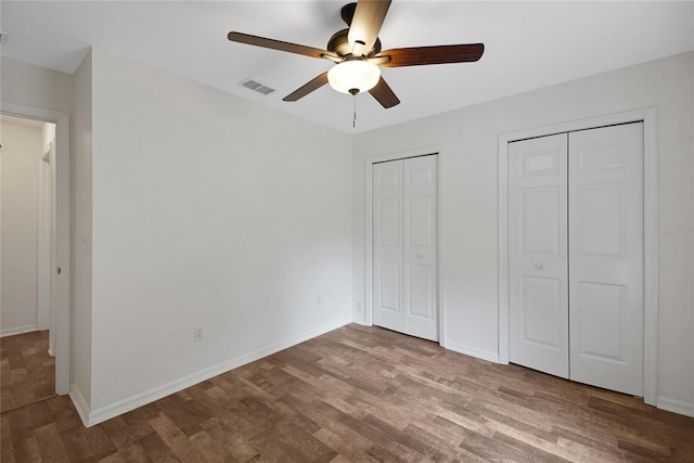 unfurnished bedroom featuring two closets, wood finished floors, and baseboards