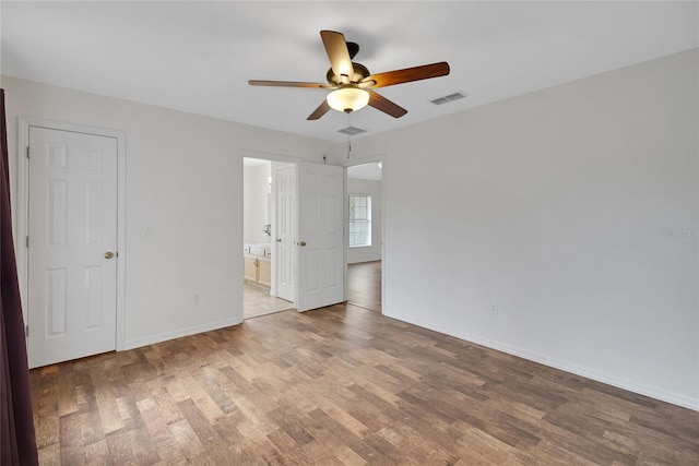 unfurnished bedroom with wood finished floors, baseboards, ensuite bath, and ceiling fan