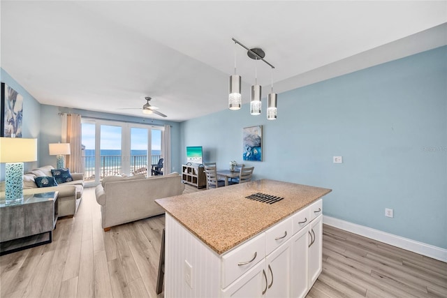 kitchen with light wood-type flooring, ceiling fan, white cabinets, hanging light fixtures, and a kitchen island
