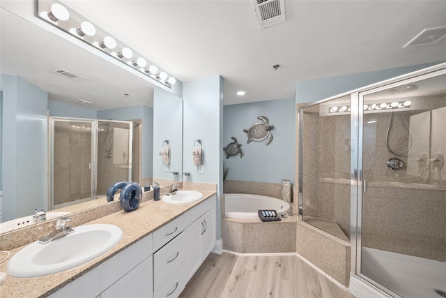 bathroom featuring a stall shower, wood finished floors, a bath, and double vanity