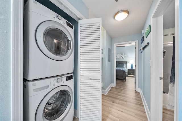 laundry area featuring stacked washing machine and dryer, light wood-type flooring, and baseboards