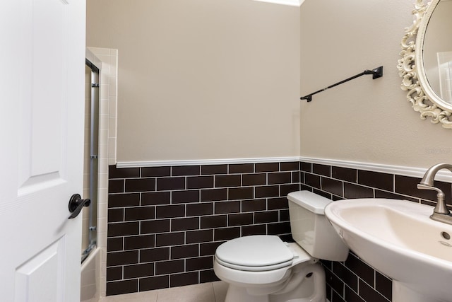 bathroom with tile walls, a sink, wainscoting, toilet, and bathing tub / shower combination