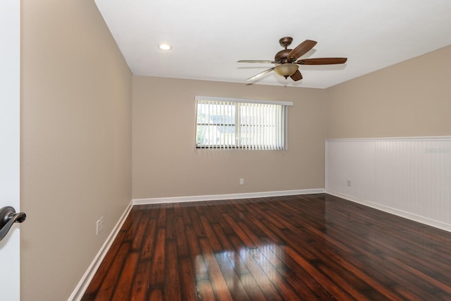 unfurnished room with dark wood-style flooring, a ceiling fan, baseboards, and wainscoting