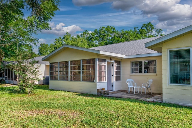 rear view of property featuring a sunroom, a lawn, a shingled roof, and cooling unit