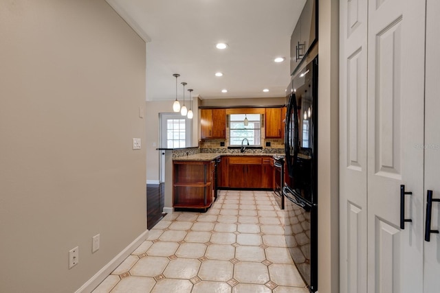 kitchen with freestanding refrigerator, recessed lighting, brown cabinets, baseboards, and light flooring